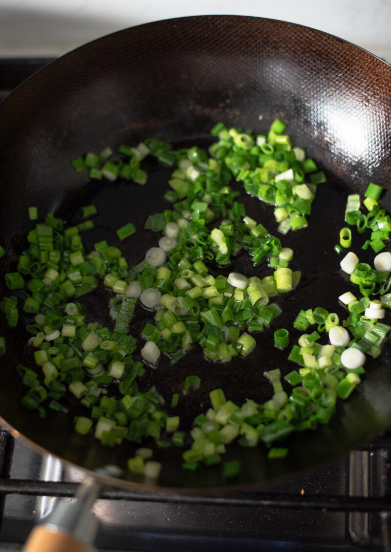 Bunch of chopped green onion are cooking in a wok.