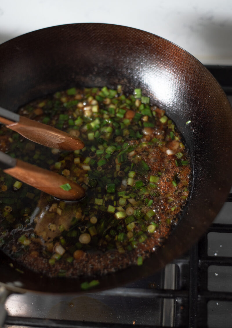 Soba noodle sauce mixture added to cooked green onion in a wok.