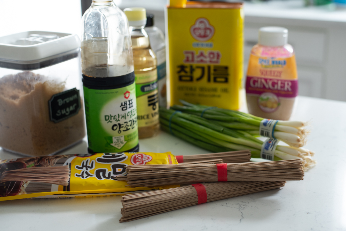 Pantry ingredients laid out for sesame soba noodles, including soy sauce, sesame oil, and green onion