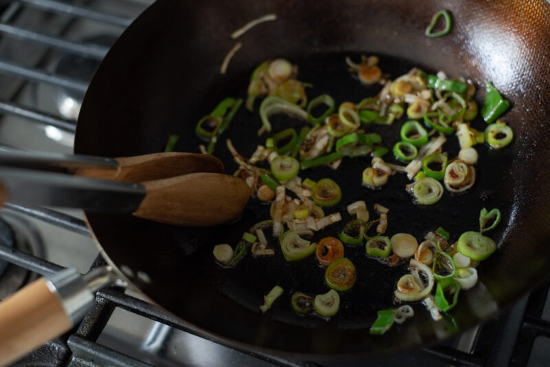 Chopped Asian leek are stir-frying in oil in a wok to make Korean spicy pork.