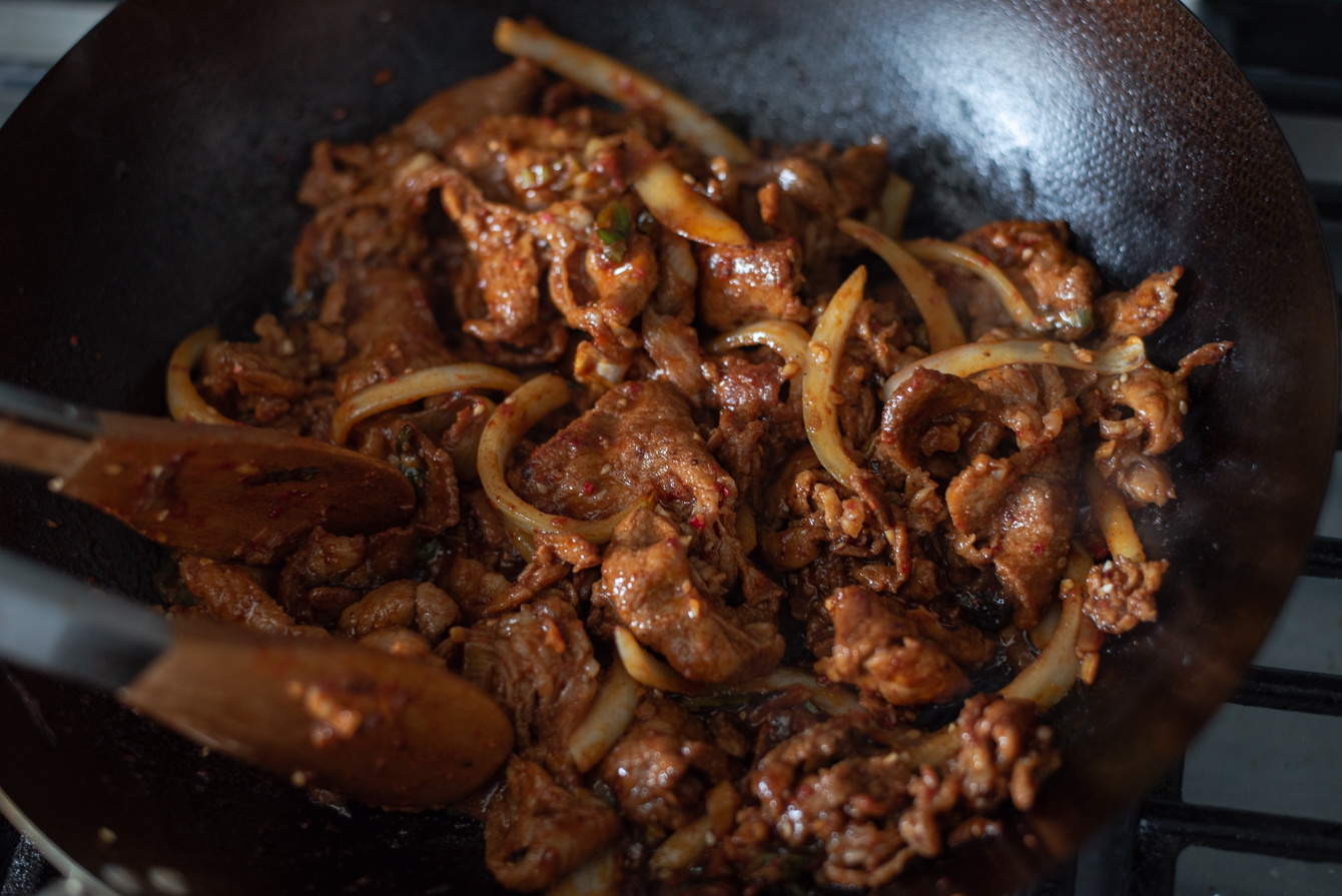 Jeyuk bokkeum stir-frying in a wok.