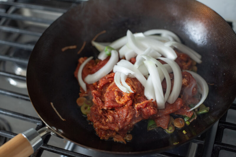 Gochujang marinated pork slices and onion are placed in a skillet over the stove.