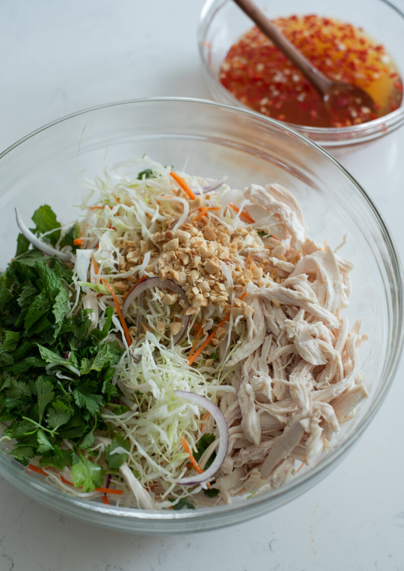 Vietnamese chicken salad ingredients are combined in a mixing bowl with fresh herbs.