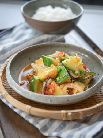 Korean round zucchini and anchovy side dish is served in a small bowl on a woven patter