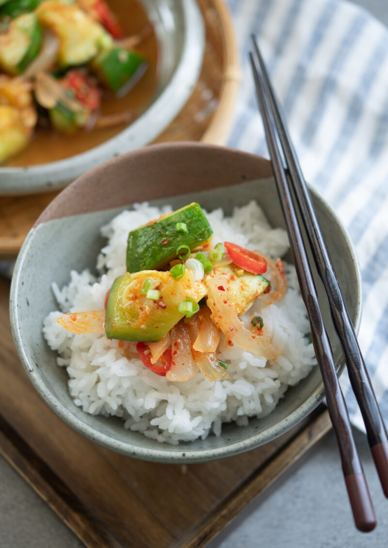 A few pieces of Korean zucchini side dish is topped over white rice in a bowl.