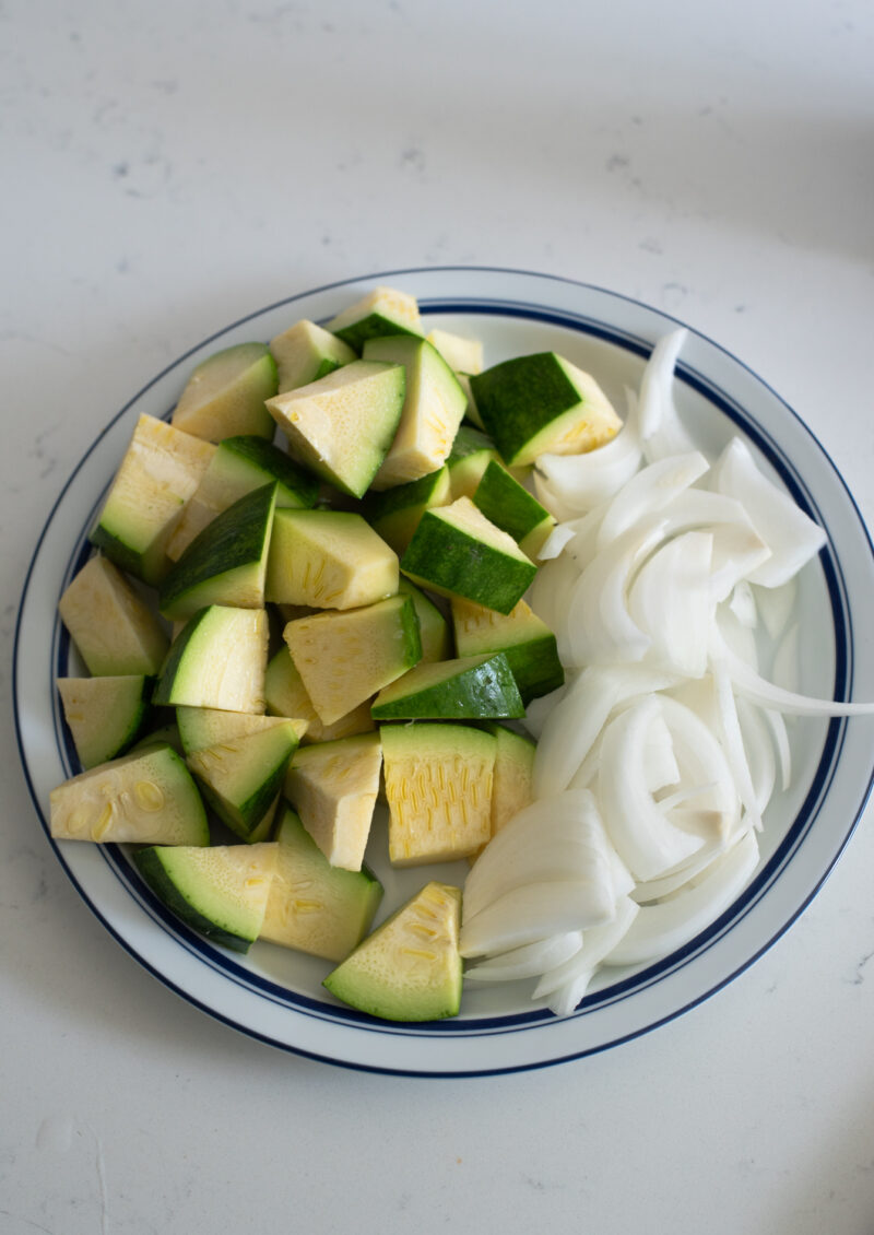 Diced zucchini and sliced onion are placed together on a blue rimmed plate.