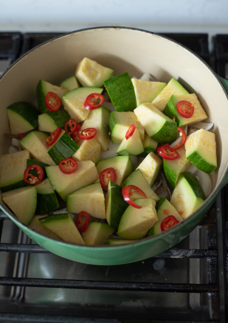 Zucchini slices are added on top of onion and dreid anchovies in a pot.