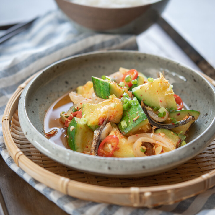 Zucchini squash and dried anchovy side dish is served on a grey plate in a woven platter