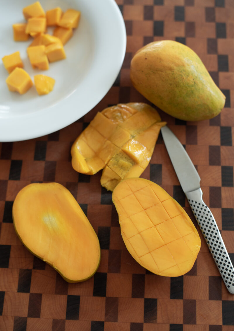 A mango is sliced away from the seed and scored with a paring knife.
