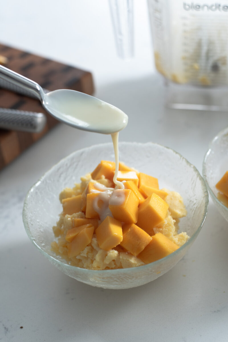 A spoonful of condensed milk drizzling over fresh mango shaved ice.