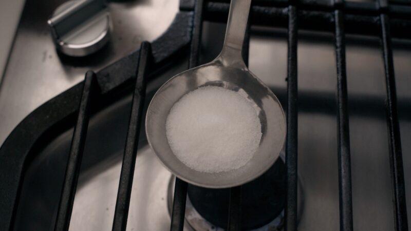 White sugar is place in a ladle over heat source on the stove.