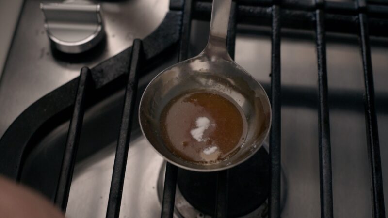 A small amount of baking soda is added to the caramelized sugar in a ladle.