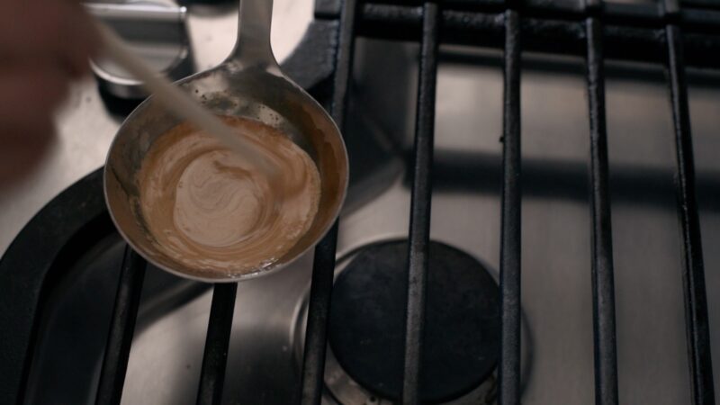 A chopstick is stirring the melted sugar and baking soda together away from the heat source.