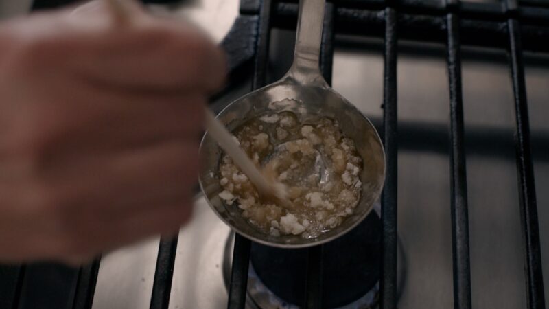 A wooden chopstick is stirring half melted sugar on the stove.