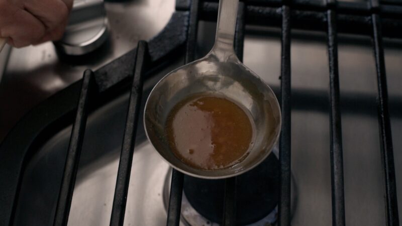 Sugar has caramelized to amber color in a ladle over stove.