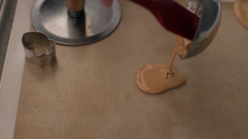 A spatula is scrapping the melted dalgona candy  from the ladle and poured on a silicon mat.