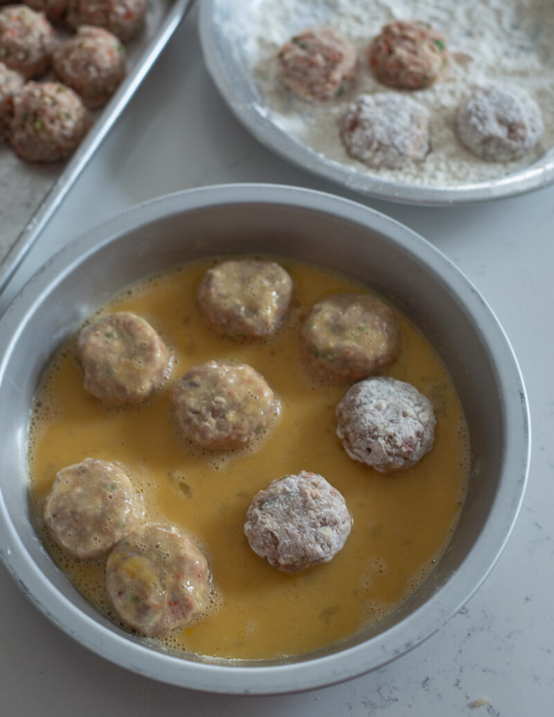 Meat patties are coated with flour, then beaten eggs in a round bowl.