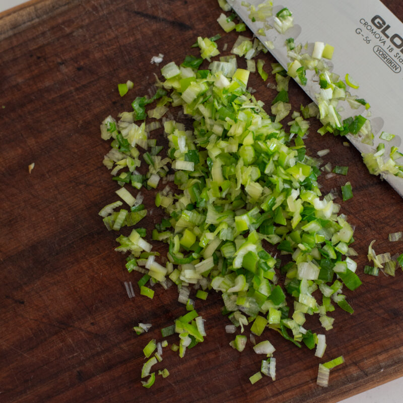A knife chopped green onion finely on a wooden board.