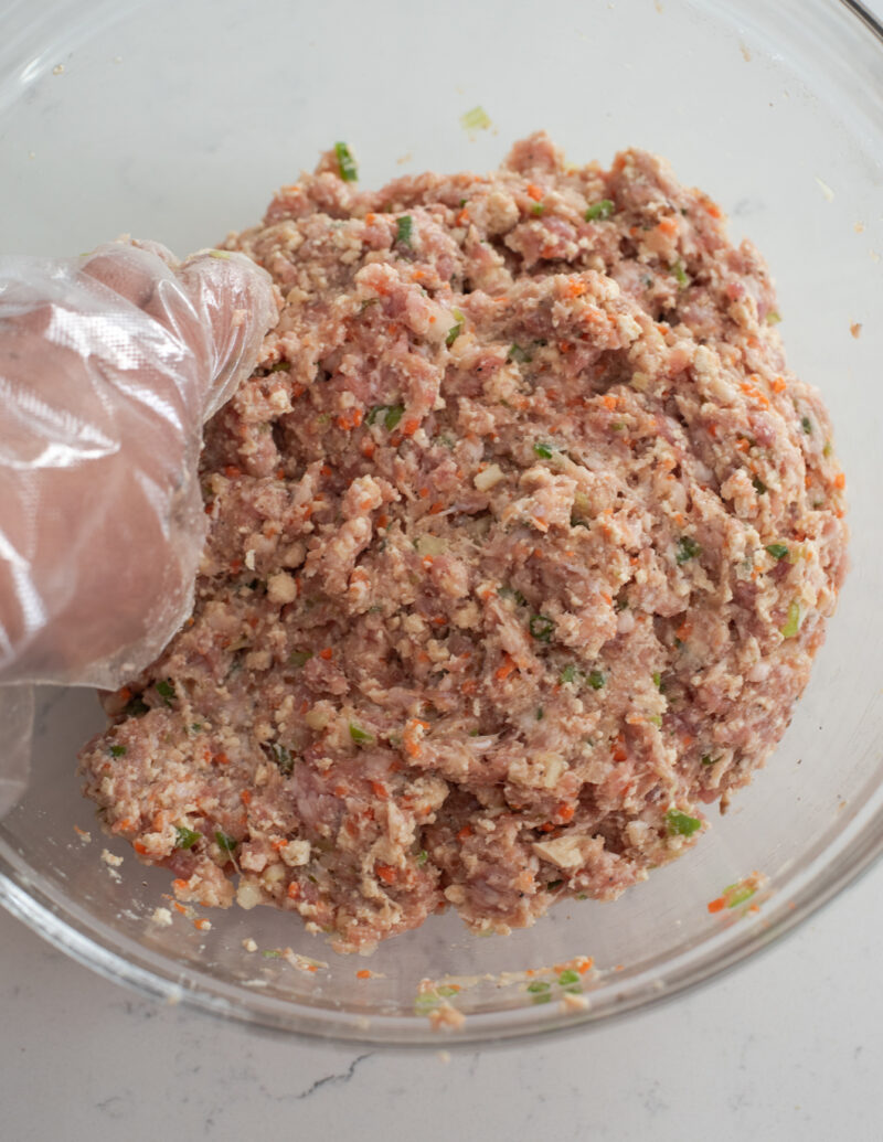 Meat and tofu patties are mixed by hand in a bowl.