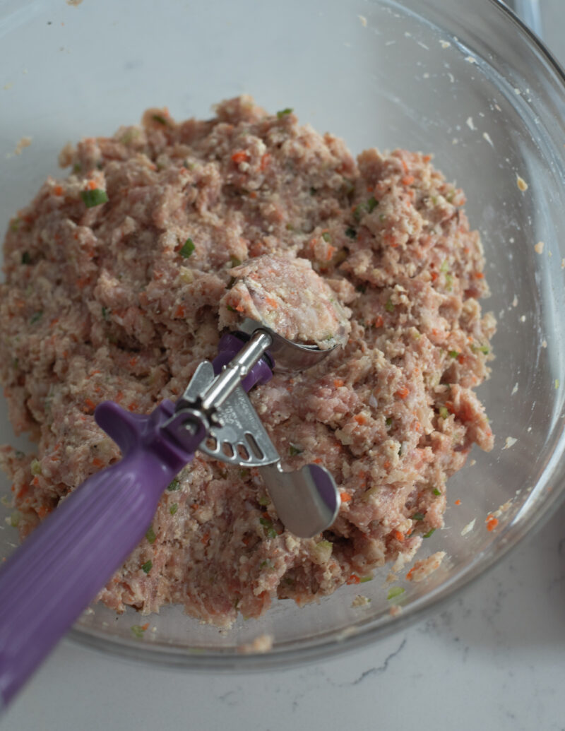 A purple cookie scoop is scooping out a portion of meat tofu patty mixture in a bowl.