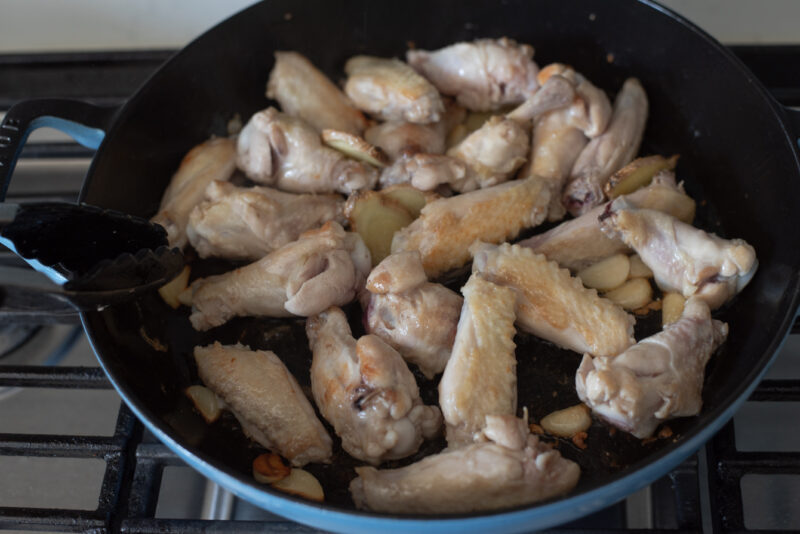 Chicken wings are browned in oil with garlic and ginger in a pan.