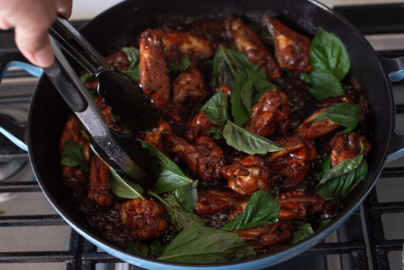 Fresh Thai basil leaves are added to Taiwanese three cup chicken in a pan.