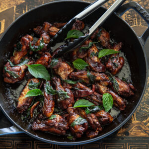Taiwanese three cup chicken wings (san bei ji) are adorned with glaze and fresh Thai basil leaves