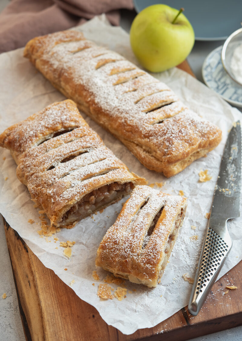 A slice of puff pastry apple strudel has flaky crust with soft apple filling inside.