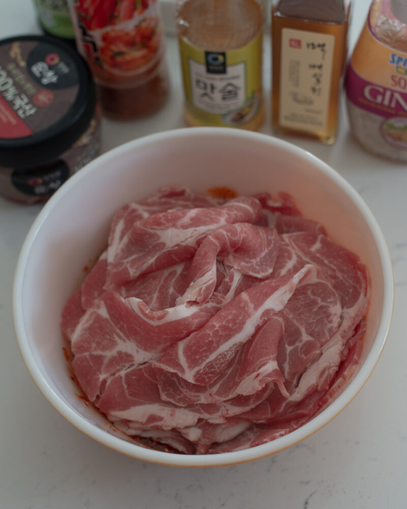 Thin slices of pork shoulder added to pork bulgogi sauce in a bowl.