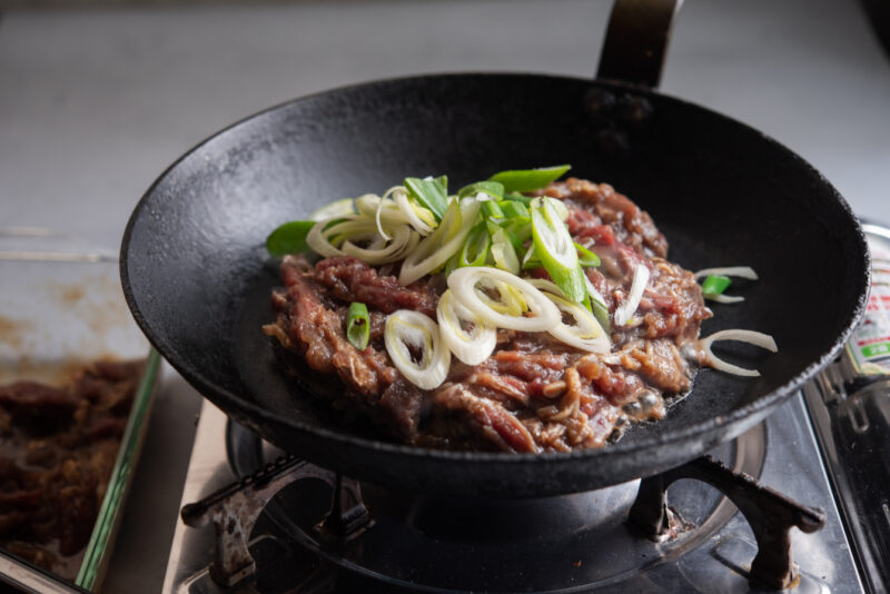 Marinated beef placed on a hot skillet.