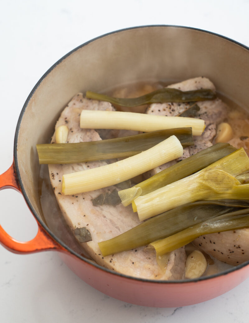 A pot of simmered pork belly topped with Asian leek is showing its doneness.