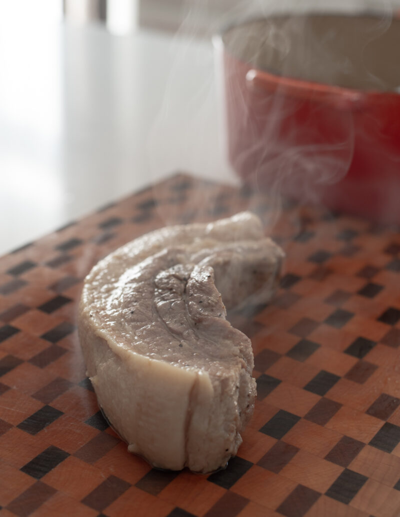 Cooked pork belly steaming on a wooden cutting board.