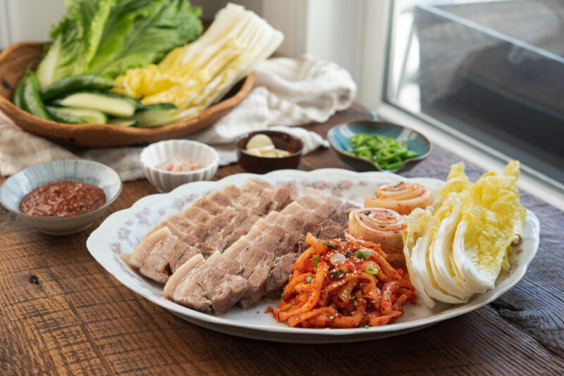 Korean bossam abd radish salad is arranged with pickled cabbage to make bossam wraps