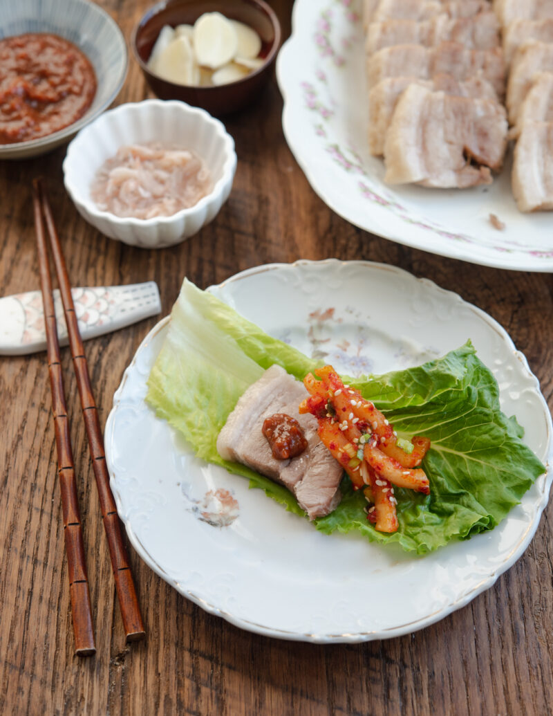 A green lettuce leaf is topped iwth bossam pork belly, radish kimchi, and ssamjang.