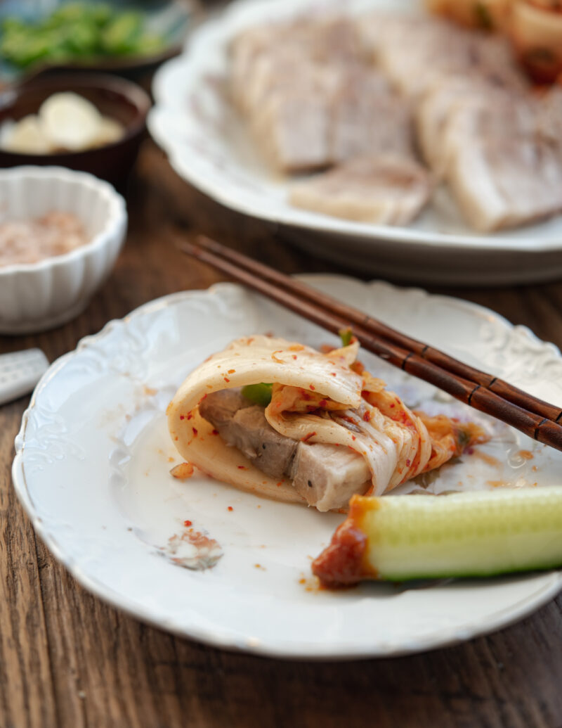 A strip of cabbage kimchi on the plate is wrapping bossam piece inside .