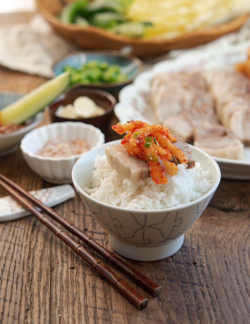 Bossam pork belly and radish kimchi placed on top of a bowl or rice.