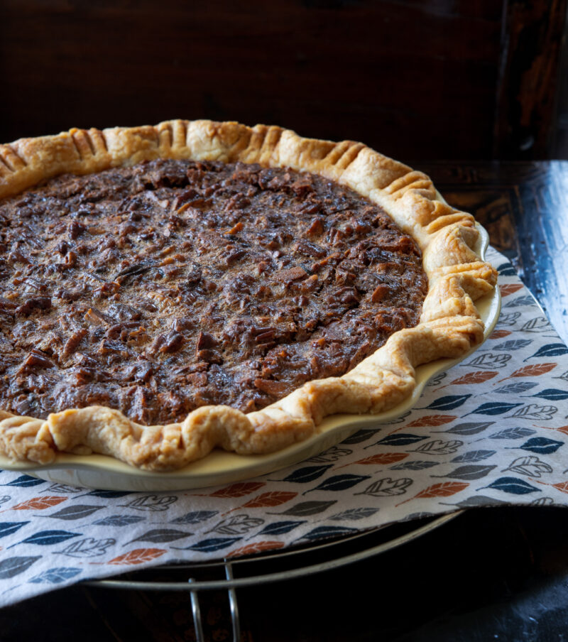 A whole butterscotch pie is resting on a cooling rack lined with leafy napkin.