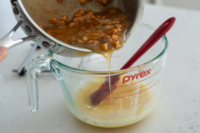 Sugar syrup and butterscotch chip mixture is poured into beaten egg in a mixture.