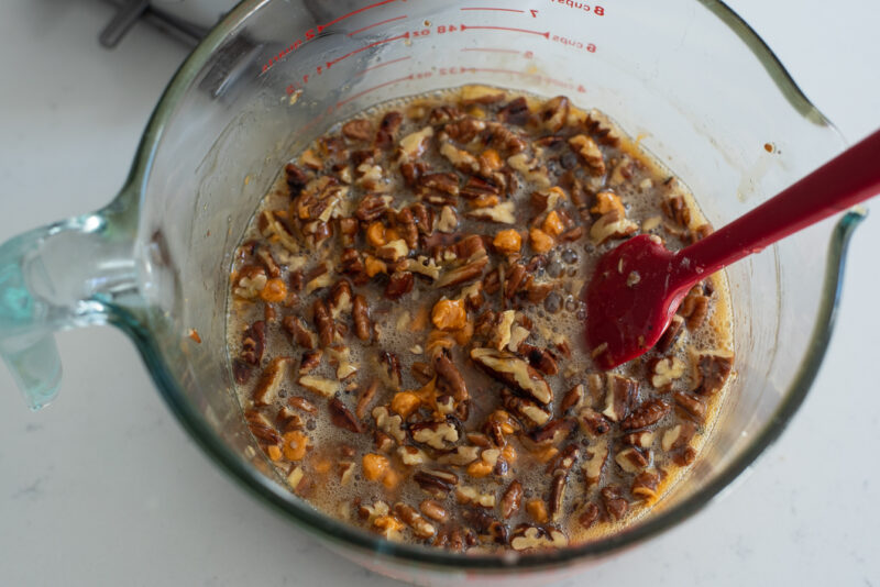 Chopped pecan pieces are added to butterscotch sugar mixture in a bowl.