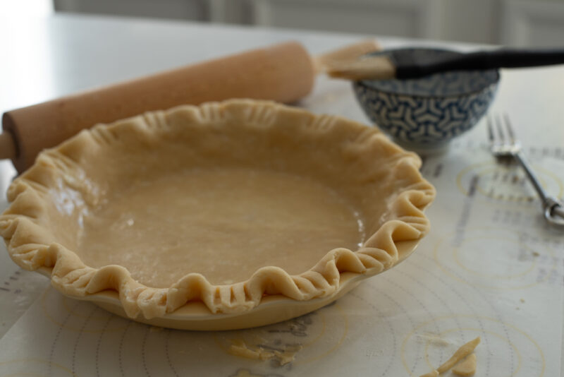 A pie crust is fluted on the edge in a pie pan.