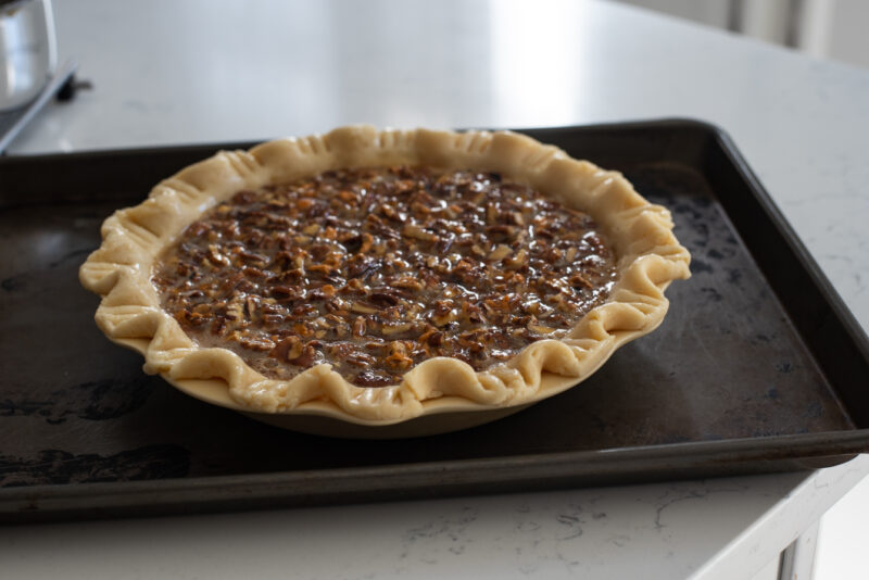 A pie pan filled with butterscotch pecan pie filling is placed on a baking sheet.