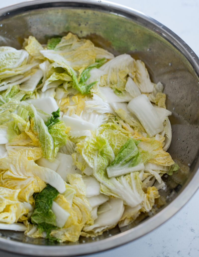 Salted cabbage pieces are showing wilted in a large bowl.