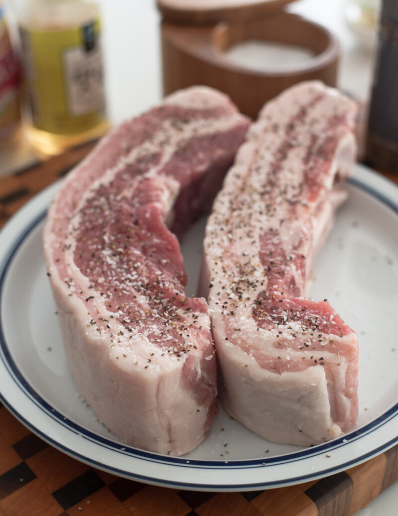 Two chunks of pork belly is seasoned with salt and pepper on top.