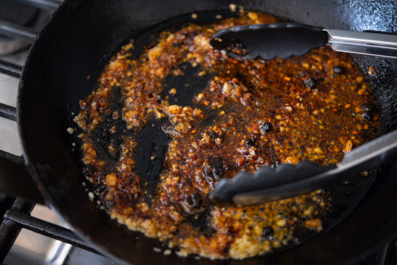 Chili crisp and garlic are fried together in oil in a skillet.