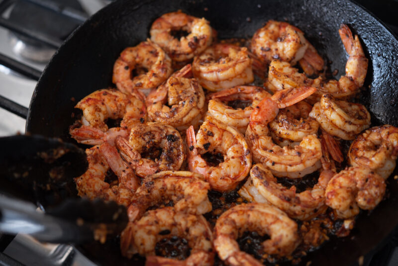 Large shrimps are added to chili crips mixture and tossed in a skillet.