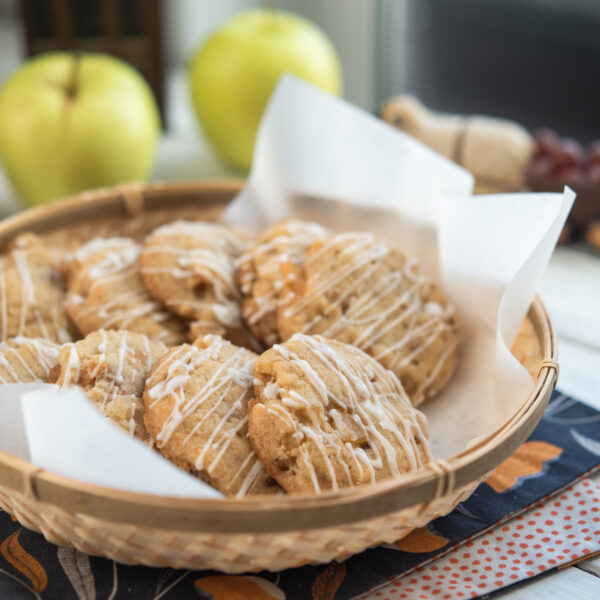 Soft apple cookies are served in a lined basket with apples behind.