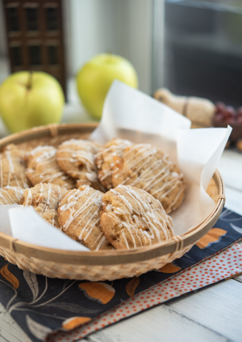 Soft apple cookies are served in a lined basket with apples behind.