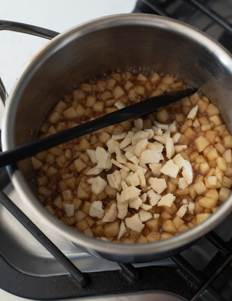 Chopped dried apple pieces are added to cooked fresh apples in a sauce pan.