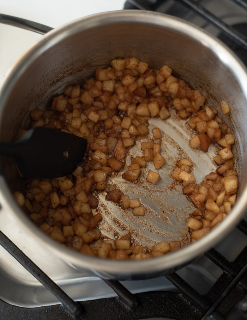 Chopped apples are cooked off in cinnamon sugar mixture in a pan.