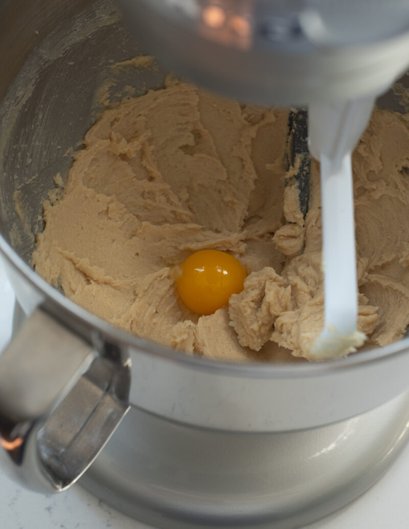 An egg yolk is added to the butter sugar mixture in a stand mixer.